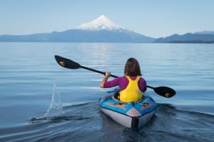 A lady on a kayak on a lake with a snow capped volcano in the background enjoying the best time to visit Chile