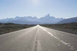 A grey road with the Fitzroy mountain range in the back. El Chalten, Argentina