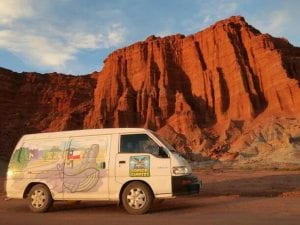 A sunset photo of a condor campervan against some glowing red rocks in talampaya, argentina