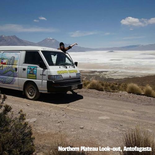 A Condor Campers Campervan at a lookout plateau, Antofagasta, Chile. A customer leans out of the window pointing to a view of clouds hanging over a flat valley.
